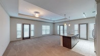 This single-story residence is designed with an open-concept layout that seamlessly connects the living area and kitchen, creating a generous and airy atmosphere. The living space features plush wall-to-wall carpeting, a distinctive tray ceiling with crown molding, a ceiling fan, and multiple windows with blinds that invite abundant natural light. Two glass-panel doors provide access to exterior balconies, further enhancing the sense of openness.

The kitchen is outfitted with dark wood cabinetry, granite-style countertops, and a large island with a built-in sink, ideal for both meal preparation and casual dining. Stainless steel appliances, including a refrigerator, range, and microwave, complement the space, while pendant lighting adds a refined touch.

The bedrooms are carpeted and well-proportioned, each featuring windows with natural views. At least one bedroom includes a walk-in closet with built-in wire shelving. A standout bedroom features a tray ceiling, adding architectural interest.

The primary bathroom offers a dual-sink vanity with granite-style countertops, dark wood cabinetry, tile flooring, and a separate shower area. A secondary bathroom includes a single-sink vanity and a tub-shower combination with subway tile surround, maintaining a consistent, modern aesthetic throughout.