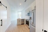 Located in Charlotte's vibrant 28205 zip code, this one-bedroom, one-bathroom unit offers a thoughtfully designed single-floor layout with a clean, contemporary aesthetic throughout. Light-toned luxury vinyl plank flooring runs consistently across all rooms, complementing the bright white walls and recessed lighting that keep the space feeling open and airy.

The kitchen is a standout feature, outfitted with two-tone gray flat-front cabinetry accented by matte black hardware, a white quartz peninsula countertop with an integrated sink, and a full suite of stainless steel appliances including a French door refrigerator, electric range, over-the-range microwave, and dishwasher. A white subway tile backsplash adds a clean, classic detail. Natural light filters in through a window adjacent to the peninsula, connecting the kitchen visually to the living area.

The bedroom is a calm, neutral space with white walls, natural light from a high window, and ample room for furnishings.

The bathroom is finished with marble-look porcelain tile surrounding a soaking tub and shower, paired with a white vanity countertop, gray cabinetry, and matte black fixtures and accessories throughout, creating a cohesive, modern feel.