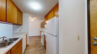 Located in Little Canada, Minnesota, this two-bedroom, two-bathroom residence offers a practical and well-organized single-floor layout. The galley-style kitchen is appointed with warm honey-toned wood cabinetry, light wood-style flooring, and white appliances including a range, refrigerator, and dishwasher. A ceiling fan overhead and generous upper and lower cabinet storage make this an efficient and functional cooking space. The kitchen flows into a combined dining area featuring additional wood cabinetry with glass-front uppers, providing both display and storage options. The living room is a bright, open area highlighted by a large sliding glass door that opens to a private balcony with outdoor views, allowing natural light to fill the space. Soft carpeting and a textured ceiling carry throughout the living and bedroom areas. The generously sized primary bedroom includes sliding wood-panel closet doors, while the second bedroom benefits from a wide window with natural light and a baseboard heating system. Both bedrooms offer comfortable proportions and individual closet access. The two bathrooms are finished with classic mosaic tile flooring, wood-toned vanities, and tub-shower combinations. A hallway connects the rooms efficiently, and four total closets provide abundant storage throughout the residence.