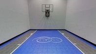 This single-level indoor basketball court offers a dedicated space for sport and recreation. The playing surface features interlocking sport tiles in bold blue, accented by grey bordering tiles and crisp white court markings. A prominent CityWest logo is displayed at center court, adding a branded identity to the space. A wall-mounted glass backboard with a standard hoop is installed at one end, positioned against a smooth, light grey painted wall. The clean, minimalist design of the surrounding walls keeps the focus on the court itself. The space is well-suited for casual play, skill development, or organized recreational activities. The enclosed environment provides a controlled setting, unaffected by outdoor conditions, making it usable year-round. The layout and court markings suggest thoughtful planning to maximize the functional playing area within the space. Overall, the court presents a professional and polished appearance, combining practical sport infrastructure with a clean aesthetic that reflects a well-maintained recreational facility.