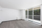 This single-floor unit offers a straightforward, functional layout designed to maximize the use of available space. The living area is finished with neutral-toned carpet and features wall-mounted sconce lighting that provides a warm, even glow throughout the room. A low-profile cabinet unit sits along one wall, and drape-covered windows allow for natural light while maintaining privacy.

The kitchen is efficiently arranged in an L-shaped configuration, outfitted with warm wood-toned cabinetry that extends to the ceiling for ample storage. White appliances, including a full-size refrigerator, electric range, and under-cabinet range hood, are accompanied by a single-basin sink with a modern faucet. The kitchen floor transitions to a wood-look surface, distinguishing it from the carpeted living space.

A hallway connects the main living area to the rest of the unit, where a sliding-door closet with a built-in hanging rod provides convenient clothing storage. Additional built-in drawers and shelving are visible nearby, offering further organizational options.

The bathroom features wood-look flooring, a wall-mounted sink, a mirrored medicine cabinet, and a full bathtub with yellow-tiled surround, completing the unit's practical and no-frills design.