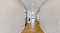 This thoughtfully designed single-floor amenity space offers a generous layout with distinct zones for lounging, dining, and recreation, all unified by warm wood-look flooring, neutral gray walls, and recessed lighting. The wide hallways are lined with sleek black-framed glass doors and frosted panels, creating a clean, modern entryway experience that connects seamlessly to the interior gathering areas.

The living room serves as the social heart of the space, furnished with rich cognac leather sofas, layered area rugs, and an eye-catching gallery wall of colorful contemporary art. Adjacent to it, a stylishly appointed wet bar area features navy cabinetry with a white countertop, a beverage refrigerator, and two bold statement wallpapers — one with sweeping teal abstract lines and another with a geometric diamond pattern — adding vibrant personality to the room.

The combined dining and lounge area offers flexible seating options, including a built-in green banquette booth with pedestal tables and a bar counter with modern black stools. The game room is a standout feature, centered around a full-size pool table beneath a gold crystal chandelier, with abundant natural light streaming through large windows. Together, these spaces create a dynamic, welcoming environment ideal for community gathering and recreation.