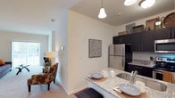 This single-story residence offers a thoughtfully designed layout that balances functionality and comfort throughout its principal living spaces. The kitchen is a standout feature, outfitted with dark espresso cabinetry extending to the ceiling, granite-patterned countertops, stainless steel appliances including a refrigerator, electric range, and microwave, and durable hardwood-style flooring. A peninsula with seating provides a natural transition into the adjacent living and dining areas, which feature plush carpeting and neutral walls that create a warm, cohesive atmosphere.

The living room is generously proportioned, with sliding glass doors fitted with vertical blinds that open to an outdoor area and invite natural light. A separate dining area accommodates a full-sized table and is conveniently positioned near the kitchen. Two bedrooms, each finished with soft carpet and bright windows, offer comfortable retreats. The primary bedroom connects directly to a bathroom featuring a granite-topped vanity with white cabinetry and a walk-in shower. A second full bathroom mirrors this finishes with a tub-shower combination and tile-style flooring, accessible from the hallway.