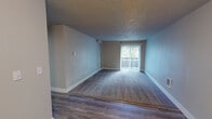 Located at 25920 112th Ave SE in Kent, Washington, this single-floor residential unit offers a well-organized layout designed for comfortable everyday living. The open living area is a standout feature, with plush carpeting, neutral gray walls, and a textured ceiling. A sliding glass door leads to a private balcony, allowing natural light to fill the space and providing outdoor views of the surrounding community.

The kitchen is thoughtfully appointed with dark wood-grain lower cabinetry, crisp white upper cabinets, and clean white countertops. A white tile backsplash complements the stainless steel appliances, which include an electric range and an over-the-range microwave. Wood-look vinyl flooring runs through the kitchen and entry areas, creating a seamless transition between spaces.

The bedroom features soft carpeting, a window with blinds that brings in natural light, and a baseboard heater. The neutral tones throughout maintain a calm, cohesive aesthetic. The bathroom includes a full tub and shower combination with chrome fixtures, complemented by tile flooring. A dedicated hallway connects the main living areas to the private spaces, contributing to an efficient and functional floor plan overall.