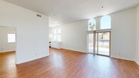 This single-floor unit offers a thoughtfully designed layout filled with natural light and clean, modern finishes throughout. Warm hardwood flooring flows seamlessly across every room, complementing the crisp white walls and creating a bright, cohesive atmosphere.

The open living area is a standout, featuring soaring ceilings and dramatic arched windows that flood the space with sunlight while framing outdoor views of palm trees and the surrounding neighborhood. A sliding glass door leads to a private balcony, extending the living space outdoors. High clerestory windows further enhance the airy, open feel.

The kitchen is efficiently designed in a galley style, featuring white cabinetry, light stone-finish countertops, a double sink, stainless steel appliances including a refrigerator and range, and ample storage. Large windows above the counter bring in generous natural light.

The bedrooms are generously proportioned with tall ceilings, elevated windows for privacy and light, and closet access. The two bathrooms are finished in a clean, contemporary style — one featuring a tub-shower combination with classic subway tile, a white vanity with stone countertop, and overhead cabinetry; the other a simpler half-bath configuration with matching finishes. The overall ambiance is light, airy, and move-in ready.
