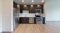 Located at 81 Arch St in Hartford, Connecticut, this single-floor unit offers a thoughtfully designed layout with a clean, contemporary aesthetic throughout. Light-toned hardwood flooring flows consistently across the main living areas, creating a bright and cohesive feel that complements the crisp white walls and recessed lighting overhead.

The open living area is filled with natural light courtesy of large, multi-pane black-framed windows that frame views of the surrounding neighborhood's treetops and cityscape. The space feels airy and well-proportioned, with ample room for flexible furniture arrangements.

The kitchen is a standout feature, outfitted with rich dark espresso cabinetry — both upper and lower — contrasted against white countertops and a white subway tile backsplash. A full suite of stainless steel appliances, including a refrigerator, electric range, over-the-range microwave, and dishwasher, provides a complete and functional cooking environment. The light hardwood flooring continues seamlessly into the kitchen.

The bathroom is finished with large-format gray tile flooring, white cabinetry with a granite-topped vanity, an illuminated mirror, and clean, neutral walls — delivering a polished and functional space. Additional features include a louvered double-door closet, an electrical panel, and convenient entry storage near the front door.
