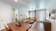 This single-floor residence offers a thoughtfully designed open layout with wood-look flooring throughout. The living area is bright and welcoming, featuring a ceiling fan, large windows with blinds, and a glass-panel door providing access to an outdoor area. Abstract artwork and neutral-toned furnishings contribute to the space's relaxed, contemporary aesthetic.

The kitchen is outfitted with white shaker-style cabinetry, white quartz countertops, stainless steel appliances including a dishwasher, range, and refrigerator, and a deep undermount sink positioned beneath a window. An island provides additional counter space and reinforces the kitchen's clean, modern look.

The bedrooms each feature distinctive teal accent walls, ceiling fans, and natural light from well-sized windows dressed with sheer curtains. One bedroom includes a walk-in closet with double hanging rods and built-in shelving, offering generous storage. The bathroom includes a white vanity with ample counter space and connects to a laundry closet with a stacked washer and dryer. A hallway leads to additional bathroom access, with wood-look flooring continuing seamlessly throughout the private areas of the residence.