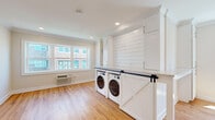 Located at 70 Polifly Rd in Hackensack, NJ, this efficiently designed single-floor unit makes excellent use of its intimate footprint. The open layout is anchored by warm hardwood flooring that runs throughout the main living area, complemented by crown molding, recessed lighting, and neutral wall tones that contribute to a bright, clean aesthetic.

The kitchen is a standout feature, showcasing white shaker cabinetry that extends floor to ceiling, stone-look countertops, a shiplap accent wall, and stainless steel appliances including a refrigerator and dishwasher. A sliding barn door with black hardware adds a charming design detail while concealing a full-size in-unit washer and dryer — a highly functional and thoughtful inclusion. Natural light pours in through large windows, enhancing the airy feel of the space.

The bathroom is finished in a clean, modern style with large-format tile flooring, a soaking tub with tiled surround and built-in shelving, a floating dark wood vanity with a white countertop, and a mirrored medicine cabinet. Brushed nickel fixtures complete the refined look.

The main living area is open and versatile, offering a blank canvas for a variety of configurations. Recessed lighting and crown molding elevate the overall finish of this well-maintained unit.