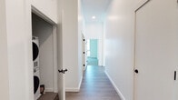 Located at 144 Addison St in Boston's East Boston neighborhood, this single-floor residence showcases a clean, modern design throughout. The open-concept living and dining area is a standout feature, highlighted by floor-to-ceiling windows on multiple walls that flood the space with natural light and offer views of the surrounding neighborhood. Light-toned hardwood flooring runs through the main living areas, and recessed lighting adds a polished, contemporary feel. A glass door leads directly to a private balcony, extending the living space outdoors. The kitchen is thoughtfully appointed with flat-front light wood cabinetry, dark stone countertops, a matte black gooseneck faucet, and stainless steel appliances including a range, dishwasher, and refrigerator. A clean, wide hallway with additional hardwood-style flooring connects the living areas to the private rooms. The bedrooms feature neutral carpet and large windows that bring in ample daylight. Two bathrooms serve the unit: one with warm terracotta tile flooring, a tub-shower combination with vertically tiled surround and matte black fixtures, and another with a glass-enclosed walk-in shower and matching matte black hardware. The overall aesthetic is modern and minimalist throughout.