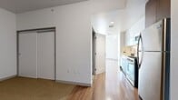 This 490 square foot apartment, located on the 8th floor at 3033 Wilshire Blvd in Los Angeles, offers a blend of compact living and modern amenities. The space is efficiently designed with an open-plan layout, maximizing the available area. The living room is a highlight, boasting warm wooden flooring that extends throughout the apartment, creating a sense of continuity and warmth. Large floor-to-ceiling windows dominate one wall, flooding the space with natural light and providing stunning views of the Los Angeles cityscape.

The bathroom is well-appointed, featuring a modern design with clean lines. It includes a combined bathtub and shower unit with a curved shower rod, a toilet, and built-in shelving for storage. The neutral color palette of white tiles and walls contributes to a sense of spaciousness and cleanliness.

The apartment's layout includes a separate area that could serve as a sleeping nook or home office, cleverly integrated into the overall design. The kitchen, while not visible in the images, is likely compact and efficient, fitting seamlessly into the open-plan design. Overall, this apartment offers a contemporary living space that maximizes functionality and style within its urban setting.
