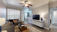 This single-story residence offers a thoughtfully designed layout with consistent wood-style flooring and crown molding throughout. The living room serves as the focal point of the home, featuring a ceiling fan, large windows with natural light, a built-in bookcase with display shelving, and direct sightlines to both the dining area and kitchen. A secondary entrance door in the living room adds convenient access.

The galley-style kitchen is equipped with dark cabinetry, granite countertops, stainless steel appliances, and an undermount sink. It opens directly into the dedicated dining area, which features a pendant light fixture and large windows dressed with bold patterned curtains.

The bedroom is a comfortable retreat with a ceiling fan, a generously sized window, and a walk-in closet outfitted with wire shelving and organizational units. The bathroom features an extended dual-sink vanity with dark wood cabinetry, white countertops, a large framed mirror, and a separate vanity seating area. A dedicated laundry space accommodates a full-sized side-by-side washer and dryer with overhead wire shelving for additional storage.