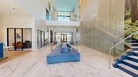 Renata's amenity space is an extensively appointed community facility spanning a generously sized single floor. The grand entrance lobby immediately establishes the design tone, featuring dramatic double-height ceilings, polished marble-look tile flooring, and a striking floor-to-ceiling metallic chain curtain installation framing a nature-inspired mural. A bold cobalt blue reception desk bearing the Renata branding serves as the welcoming focal point, accompanied by large floor-to-ceiling glass doors that invite abundant natural light and outdoor views.

The main lounge area transitions seamlessly from marble tile to wide-plank hardwood flooring, furnished with contemporary seating arrangements beneath soaring ceilings and expansive black-framed window walls overlooking a pool courtyard. A dedicated social lounge features an artistic chandelier, a communal dining table, a built-in wet bar, and an eclectic textured accent wall with integrated media displays.

The game room is well-equipped with a professional billiards table, cork flooring, a textured tile feature wall, pendant lighting, a wet bar with seating, and a wall-mounted television. An additional activity room includes a quartz-topped island, blue accent seating, and a shuffleboard table. A staircase with sleek metal railings connects to an upper-level overlook, completing this sophisticated amenity environment.