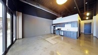 This single-floor urban loft showcases a striking industrial-modern aesthetic that makes a bold architectural statement. The open-concept layout is anchored by polished concrete floors that reflect light across the expansive main living area, lending the space a sleek, contemporary character. Soaring ceilings finished in dramatic matte black add depth and visual contrast, while exposed structural elements reinforce the industrial design language throughout.

The kitchen is positioned along one wall and is thoughtfully appointed with dark navy cabinetry that runs the full length of the space, paired with a clean white backsplash for crisp contrast. Stainless steel appliances — including a refrigerator, electric range, built-in microwave, and dishwasher — provide a fully functional and modern culinary setup. A stainless steel sink with a contemporary faucet completes the kitchen's clean, professional finish.

Pendant lighting and recessed fixtures illuminate the space with warm tones, enhancing the loft's inviting ambiance despite its industrial roots. The generous open floor plan offers remarkable flexibility for a variety of living or working arrangements. The overall atmosphere is one of curated minimalism — spacious, functional, and architecturally refined, ideal for those who appreciate modern urban living.