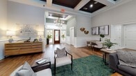 Located at 325 Marymeade Dr in Summerville, SC, this single-story community clubhouse offers a refined and welcoming atmosphere defined by thoughtful architectural details and high-end finishes throughout. The entry foyer greets visitors with elegant coffered ceilings featuring rich dark wood inlays, a statement chandelier, warm hardwood flooring, and glass-paneled front doors that invite natural light into the space. Wainscoting and sage-green accent walls add a coastal Southern charm that flows consistently through the interior. The expansive main lounge serves as the heart of the space, anchored by a floor-to-ceiling stacked stone fireplace with a mounted flat-screen TV above. Generous seating arrangements on lush botanical-print area rugs create a comfortable and social environment, while a wall of French doors floods the room with natural light and provides views of the surrounding exterior. A bar-height counter area and a sleek galley-style kitchenette offer a marble-look quartz countertop, white shaker cabinetry, and stainless steel appliances, making the space well-suited for gatherings and events. A dedicated seating nook near the entry provides an intimate space for meetings or casual conversation. Throughout, the consistent use of hardwood flooring, coffered ceilings, and curated décor creates a cohesive, upscale ambiance ideal for community engagement.