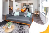 Located in the vibrant city of Ferndale, Michigan, this single-floor residence at 430 W 9 Mile Rd offers a thoughtfully designed living space with a clean, modern aesthetic throughout. The open-concept kitchen is a standout feature, showcasing light wood cabinetry, a sparkling quartz peninsula countertop ideal for casual dining or meal prep, and a full suite of stainless steel appliances including a range, microwave, and dishwasher. A pendant light adds a contemporary touch overhead. The living area is bright and welcoming, with a window that frames views of surrounding greenery, flooding the room with natural light. It comfortably accommodates a sofa, accent chair, and media console, creating a relaxed yet stylish atmosphere. The bedroom offers a calm retreat with crisp white walls, recessed lighting, and ample space for a full-sized bed. The bathroom features a clean, all-white tiled walk-in shower with built-in shelving and chrome fixtures. A dedicated utility room houses the water heater and includes overhead shelving, providing practical storage and laundry hookup potential. Wood-look flooring flows consistently throughout, tying the space together with a warm, cohesive feel.