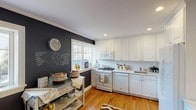 This two-floor residence at 31 Putnam Green in Greenwich, CT offers a well-designed layout across two levels. The main floor features warm hardwood flooring throughout an open living area, where large windows invite natural light and a pass-through connects to the kitchen. The kitchen is appointed with white raised-panel cabinetry, granite countertops, a subway tile backsplash, and full appliances, while a bold chalkboard accent wall adds a distinctive, functional touch. A convenient half bath on the main level features deep navy walls and classic white fixtures. Upstairs, two spacious bedrooms continue the hardwood flooring and crown molding details. The primary bedroom is distinguished by charcoal-toned walls and generous natural light from multiple windows. The second bedroom offers a more neutral palette with a closet and easy access to the full hall bathroom, which features a marble-topped vanity, tile flooring, and a tub-shower combination. Crown molding, recessed lighting, and consistent hardwood floors unify the home's aesthetic throughout both levels, creating a cohesive and comfortable living environment in one of Greenwich's established residential communities.
