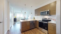 This well-appointed single-floor residence showcases a thoughtfully designed open-concept layout with contemporary finishes throughout. The kitchen serves as the heart of the home, featuring warm wood-toned cabinetry, crisp white quartz countertops, and a full suite of stainless steel appliances including a range, microwave, dishwasher, and refrigerator. A peninsula with bar seating and stylish pendant lighting overhead creates a natural gathering space and seamlessly connects the kitchen to the living area. Wood-look flooring flows continuously throughout the unit, adding warmth and cohesion to the space.

The living area is bright and inviting, benefiting from a large window that allows ample natural light and provides views of the surrounding neighborhood. A ceiling fan adds both function and style to the room.

Two comfortable bedrooms each feature large windows with expansive outdoor views, allowing natural light to fill the spaces. The bathroom is finished with striking marble-look tile in the tub and shower surround, complemented by wood-toned cabinetry for storage.

Overall, the residence strikes a balance between modern design and functional living, with clean lines, neutral tones, and quality finishes creating a bright, cohesive, and welcoming atmosphere throughout.