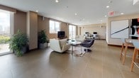This single-floor amenity space is thoughtfully designed to accommodate a variety of social and recreational activities within a cohesive, modern aesthetic. Large-format tile flooring in a warm taupe tone flows continuously throughout, unifying each functional zone while contributing to the space's clean, polished character.

The lounge area serves as a central gathering point, furnished with white and charcoal swivel chairs, contemporary sofas, and sleek coffee tables arranged around a flat-screen television. Floor-to-ceiling sliding glass doors and generous windows flood this area with natural light and frame panoramic city skyline views, creating an airy, elevated ambiance.

Adjacent to the lounge is a billiards zone featuring a pool table alongside a casual seating arrangement of two swivel chairs and a round side table, accented by a bold red abstract painting. A high-top bar and dining area offers wood-paneled bar counters with pendant lighting and bar-height seating.

The kitchenette is equipped with light wood cabinetry, a sink with a grey countertop, and a wall-mounted television, supported by commercial-grade doors for ease of access. A separate high-top table dining section opens directly to an outdoor terrace, extending the social space outdoors with additional skyline views.
