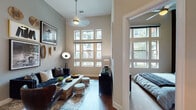 This single-floor residence makes a striking impression with its soaring ceilings and generous window arrangements that flood each room with natural light. The living area serves as the heart of the home, anchored by dramatic floor-to-ceiling window grids that frame outdoor views of the surrounding neighborhood. A tufted navy sofa, rustic wood coffee table, and curated gallery wall featuring framed artwork and woven decorative accents lend the space a sophisticated yet eclectic personality. Hardwood flooring flows throughout the main living areas, adding warmth and continuity.

The kitchen is well-equipped with rich espresso-toned cabinetry extending to the upper reaches of the tall walls, a distinctive wine rack detail, stainless steel appliances including a refrigerator, range, and microwave, and light quartz countertops complemented by a classic tile backsplash.

The bedroom is a tranquil retreat, featuring large multi-pane windows that invite ample daylight, soft carpeting, and a statement wall adorned with an arrangement of vintage bicycle wheels, adding a bold artistic touch. The bathroom continues the cohesive design with dark wood cabinetry, a wide framed mirror, and a tiled soaking tub and shower combination.