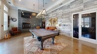 Located at 1709 Cason Ln in Murfreesboro, TN, this single-floor community lounge and billiards room offers a well-appointed gathering space with a thoughtfully designed interior. Polished concrete floors extend throughout, giving the space a sleek, modern foundation that complements the room's eclectic mix of rustic and contemporary design elements.

At the heart of the room sits a full-sized billiards table, illuminated by a striking geometric pendant light that serves as a focal point. One wall is clad in stacked stone, anchoring a built-in fireplace flanked by a wall-mounted television — creating a cozy seating area with a leather armchair and sofa. An adjacent accent wall features weathered wood-look tile, adding warmth and texture to the space.

Large double-pane windows dressed with white blinds flood the interior with natural light and offer views of the outdoor courtyard. A glass-paned double door provides direct access to the exterior. Crown molding and tall ceilings enhance the sense of openness throughout.

A dining nook near the windows features a round dark-wood table with industrial-style stools, ideal for casual seating. Decorative touches — including vintage shutters, potted greenery, and layered area rugs — complete the inviting, well-balanced atmosphere of this versatile community space.