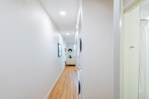 This well-appointed single-floor unit offers a clean, modern aesthetic throughout, with warm light wood flooring and recessed lighting connecting each space cohesively. The entry foyer provides a welcoming transition into the home, featuring a solid front door with a secure locking system. The open-concept living and kitchen area is bright and functional, drawing natural light through a large window that overlooks an exterior courtyard. The kitchen is efficiently designed with flat-front wood-toned cabinetry extending to the ceiling, white quartz countertops, a textured tile backsplash, stainless steel appliances including a range, over-the-range microwave, dishwasher, and refrigerator. The living area offers comfortable space for seating and entertaining, with clean lines and a neutral palette that lends itself to a variety of décor styles. The bedroom is a calm retreat, complete with a built-in closet featuring a sliding door for convenient storage. The full bathroom is finished with large-format tile flooring, a floating vanity with an integrated white basin, a backlit mirror, and a shower/tub combination. A hallway off the main living space houses a stacked washer and dryer unit, providing in-unit laundry convenience. Throughout, the space maintains a cohesive, contemporary design sensibility.