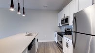Located at 223 E Town St in the heart of downtown Columbus, Ohio, this single-floor space offers a clean, contemporary design with thoughtful finishes throughout. The kitchen is a standout feature, showcasing crisp white shaker-style cabinetry with matte black hardware, light-toned countertops, and a full suite of stainless steel appliances including a range, over-the-range microwave, dishwasher, and refrigerator. A single-basin undermount sink is positioned along the kitchen island, which is accented by a sleek pendant light overhead, adding a modern touch to the space. The flooring throughout is a warm-toned wood-look plank, providing durability and visual continuity across the open layout. Neutral gray walls complement the bright cabinetry and stainless finishes, creating a balanced and inviting atmosphere. The space benefits from recessed ceiling vents, ensuring efficient climate control. The overall design aesthetic is modern and minimalist, making it well-suited for those seeking a move-in-ready space in a vibrant urban setting. Its downtown Columbus location places it within close proximity to local dining, entertainment, and professional centers.