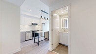 Located at 25 Gibbs Road in Toronto, this well-designed one-bedroom, one-bathroom unit offers a modern and efficient living space across a single floor. The open-concept kitchen is a standout feature, finished with sleek high-gloss white cabinetry, a subway tile backsplash, and a full suite of stainless steel appliances including a dishwasher, electric range with over-the-range microwave, and a bottom-freezer refrigerator. A central island with a light stone countertop provides additional prep space and is complemented by stylish pendant lighting, making it both functional and visually appealing. Light wood-tone laminate flooring runs throughout, adding warmth and cohesion to the space. The bedroom is a bright, tranquil retreat featuring floor-to-ceiling windows and a sliding glass door that frame sweeping views of the Toronto skyline. A mirrored sliding closet maximizes the sense of space. The bathroom is finished with large-format neutral tiles, a soaker tub with a curved shower rod, and clean chrome fixtures. The overall ambiance is contemporary and bright, with a neutral palette that creates a calm, inviting atmosphere throughout.