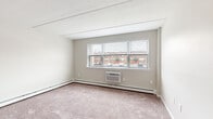 Located on S Glenwood Ave in Clifton Heights, PA, this single-floor unit offers a thoughtfully arranged layout across a compact but efficient footprint. The living area is carpeted in neutral tones and features large multi-pane windows that invite natural light and provide views of the surrounding neighborhood streetscape. A wall-mounted air conditioning unit and baseboard heating ensure year-round climate control throughout the space.

The kitchen stands out with updated grey cabinetry, subway tile backsplash, light wood-tone vinyl plank flooring, and stainless steel appliances including a refrigerator, electric range, and microwave. Baseboard heating is present here as well, adding consistent warmth to the room.

The bedroom is generously proportioned with plush carpeting and features two side-by-side double closets with louvered bifold doors, providing ample storage. An additional carpeted room with a window offers flexibility as a second bedroom or office space.

The bathroom is finished with classic white tile surrounding a full soaking tub and shower combination, complemented by a vanity with sink. Throughout the unit, neutral wall colors and tile ceilings maintain a clean, uniform aesthetic suited for comfortable everyday living.