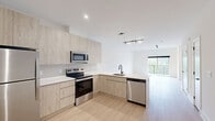 Located at 300 Furnace Street in Emmaus, PA, this thoughtfully designed two-story residence offers 1 bedroom, 2 bathrooms, and a versatile den across two well-proportioned floors. The main level features an open-concept layout where a modern kitchen flows seamlessly into the living area. The kitchen is outfitted with light wood cabinetry, stainless steel appliances including a range, microwave, and dishwasher, and a clean white countertop peninsula. Light hardwood flooring runs throughout the main level, complementing the bright white walls and recessed and track lighting. A convenient half bathroom on this floor features a floating wood-toned vanity, mirrored medicine cabinet, and matching hardwood floors. The living room opens to a private balcony offering scenic views of the surrounding greenery and rolling hills. Upstairs, the spacious primary bedroom is carpeted and features a large window overlooking lush tree canopy, a closet, and access to multiple additional closets along the hallway. The upper level also includes a full bathroom, a den, laundry, and a utility room. With six closets total, storage is plentiful throughout. The exterior showcases a contemporary building aesthetic set within a landscaped environment.