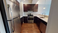 Located at 1031 John F. Kennedy Boulevard in Bayonne, New Jersey, this single-floor residence combines contemporary design with functional living. The open-concept layout connects the living area to the kitchen, creating a cohesive and welcoming environment. Rich hardwood flooring flows throughout the main living spaces, complementing the neutral-toned walls and recessed lighting overhead.

The kitchen is thoughtfully designed with dark espresso cabinetry, light quartz countertops, and a mosaic tile backsplash. Stainless steel appliances — including a gas range, refrigerator, and dishwasher — add a sleek, modern touch, while pendant lighting over the breakfast bar enhances both function and style.

The living area is bright and open, with large floor-to-ceiling windows that invite natural light and offer views of the surrounding neighborhood. A separate bedroom features plush carpeting and an expansive window with outdoor views, providing a comfortable and airy retreat.

The bathroom is clean and modern, featuring white subway tile surrounding a soaking tub and shower combination, a dark vanity with quartz countertop, a large mirror, and neutral large-format floor tiles. The overall design is cohesive, minimal, and move-in ready, making this a well-rounded residence in a convenient Bayonne location.