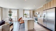 This thoughtfully designed single-floor residence offers a seamless blend of modern aesthetics and functional living. The open-concept kitchen, dining, and living area serves as the heart of the home, anchored by a generous island with bar seating, light wood cabinetry extending to the ceiling, a white tile backsplash, and a full suite of stainless steel appliances. Large windows throughout flood the space with natural light and frame pleasant outdoor views, complemented by elegant linen draping. The dining area, positioned near a bright corner window, offers a welcoming nook for meals. The living room continues the airy feel with expansive windows overlooking a balcony. Hardwood-style flooring flows consistently throughout. A well-lit hallway — accented with brass wall hooks — connects the main living areas to the private quarters. The spacious primary bedroom features a walk-in closet and opens to a dedicated bathroom finished with large-format tile flooring, wood-toned vanity cabinetry, and a tiled walk-in shower. A second full bathroom mirrors the same clean, contemporary finishes with a tiled tub-shower combination. Two closets provide ample storage throughout the residence.