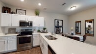 This single-floor residence offers a thoughtfully designed open-concept layout that seamlessly connects the living, dining, and kitchen areas. Rich wood-look flooring flows throughout, providing a warm and cohesive aesthetic. The spacious living room is anchored by a ceiling fan, large windows dressed with elegant drape panels that invite abundant natural light, and ample space for both lounging and a dedicated workspace. The kitchen is a standout feature, showcasing crisp white shaker cabinetry, a classic subway tile backsplash, light quartz countertops, a double-basin sink, and a full suite of stainless steel appliances including a range, over-the-range microwave, refrigerator, and dishwasher. A generous island provides additional prep space and casual seating. The bedroom is a serene retreat, complete with a ceiling fan, large windows with exterior views, and direct access to a walk-in closet. The bathroom features white cabinetry with quartz countertops, a combined tub and shower, and the same durable wood-look flooring that carries throughout the home. Every room reflects a modern, functional design that balances comfort and style.