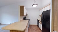 Located at 1259 Muirwood Drive in Zanesville, Ohio, this single-floor residence offers a practical and comfortable living environment. The kitchen is a standout feature, designed with functionality in mind. It showcases a galley-style layout with an extended countertop that provides generous prep and serving space. White cabinetry with warm wood-toned accents lines both sides of the kitchen, offering abundant storage from floor to ceiling. Black appliances, including a range, dishwasher, and refrigerator, lend a clean, modern contrast to the light-colored countertops. Wood-style plank flooring runs throughout the kitchen, adding warmth and durability underfoot. A pendant light fixture is centrally mounted, providing focused overhead illumination that brightens the space effectively. The clean white walls keep the interior feeling open and neutral, offering a versatile backdrop for a variety of décor styles. The single-floor layout ensures easy accessibility throughout the home, making it a practical choice for a wide range of occupants. Overall, the space presents a well-organized, move-in ready environment with a straightforward, functional design.