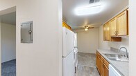 Located at 11501 Dorchester St in Southgate, Michigan, this two-bedroom, one-bathroom single-floor unit offers a practical and functional layout. The galley-style kitchen is well-appointed with warm honey-toned wood cabinetry on both upper and lower levels, gray laminate countertops, a stainless single-basin sink, a white electric coil range, and a full-size refrigerator. Light-tone wood-look flooring runs through the kitchen, transitioning to carpet in the living and bedroom areas. A ceiling fan with a light fixture provides comfort in the main living area, which also benefits from natural light through a window. The primary bedroom is generously sized and features a large window with vertical blinds that allow natural light to filter in, along with access to a dedicated closet. The second bedroom is carpeted and illuminated by a ceiling light fixture. The full bathroom includes a wood-tone vanity with a white countertop, a wide mirror with a lighted bar above, and wood-look flooring. A utility room provides additional functional space. The unit also includes a hallway and a closet, offering convenient storage throughout.