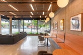 Located at 2650 Telegraph Ave in Berkeley, CA, this single-floor commercial space offers a thoughtfully designed interior that balances modern industrial aesthetics with warm, natural materials. The expansive main area is anchored by a dramatic slatted wood ceiling with integrated linear lighting and pendant fixtures, creating a visually rich overhead feature that draws the eye upward. Polished concrete floors extend throughout, lending a clean, contemporary feel underfoot.

Floor-to-ceiling glass along the storefront facade floods the interior with abundant natural light and provides open views onto Telegraph Avenue and the surrounding streetscape, creating a strong visual connection to the urban environment outside. Exposed concrete columns and accent walls add a raw, architectural texture that contrasts beautifully with the warm wood tones above.

The main lounge area features a generous sectional sofa arrangement over a patterned area rug, ideal for relaxed gathering or informal meetings. A dining and seating zone with wooden built-in benches, round tables, and modern chairs occupies one side of the space, accented by globe pendant lights and curated wall art. A secondary area includes a large wooden conference table beneath a sculptural woven pendant light, flanked by tall windows with street views—perfect for collaborative work or presentations. The overall ambiance is open, inviting, and professionally refined.