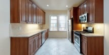 This single-floor residence offers a thoughtfully designed layout that balances classic charm with modern updates. The entryway welcomes visitors with warm hardwood flooring featuring a decorative border inlay, setting an inviting tone throughout the home.

The galley-style kitchen is a standout feature, lined on both sides with rich, dark wood cabinetry offering generous storage. Granite-topped counters complement the stainless steel appliance suite, which includes a gas range, built-in microwave, dishwasher, and refrigerator. Diagonal tile backsplash and light tile flooring complete the polished look, while a window at the end of the kitchen brings in natural light.

The living and bedroom spaces are finished with gleaming hardwood floors — some rooms showcasing classic parquet patterns — and are bathed in natural light through multiple windows. Crown molding and tall baseboards throughout add architectural character and a refined aesthetic. A radiator in one of the rooms speaks to the building's heritage while providing efficient heating.

The full bathroom is cleanly renovated, featuring floor-to-ceiling neutral tile surrounding the tub and shower combo with a sliding glass enclosure. A wood vanity with a white countertop and a mirrored medicine cabinet provide functional storage. The overall ambiance of the space is bright, clean, and move-in ready.