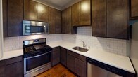 Located at 1205 Hawthorne Ave in the heart of Minneapolis, MN, this single-floor unit combines classic character with modern updates. Rich, dark hardwood flooring flows consistently throughout the living areas and bedrooms, adding warmth and a timeless aesthetic to the space.

The open living area is well-lit by multiple windows fitted with blinds, allowing natural light to filter in while offering views of mature trees outside. Cast-iron radiators provide efficient heating, and a wall-mounted air conditioning unit ensures year-round comfort. Neutral gray walls create a clean, versatile backdrop throughout.

The updated kitchen is a standout feature, offering dark wood cabinetry that extends to the ceiling for ample storage, crisp white quartz countertops, a classic white subway tile backsplash, and a full suite of stainless steel appliances including a gas range, microwave, and dishwasher. A stainless steel sink with a modern faucet completes the functional workspace.

The bedroom is generously sized with access to a walk-in closet featuring built-in hanging rods. The bathroom showcases floor-to-ceiling white subway tile in the tub surround, a natural-light window, and clean, classic finishes. The overall ambiance of the space is cozy yet functional, blending vintage architectural details with thoughtful modern updates.