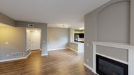 This single-floor residence is designed with an open-concept layout that connects the living, dining, and kitchen areas seamlessly. Warm wood-style flooring runs throughout the main living spaces, complemented by neutral gray walls and crisp white trim. A fireplace with a classic white mantel anchors the living area, adding a focal point to the expansive room. The kitchen is well-appointed with dark espresso cabinetry, light granite countertops, stainless steel appliances including a refrigerator and microwave, and a peninsula with a double sink that doubles as a breakfast bar. Natural light filters in through multiple windows, including a large window in the kitchen overlooking the outdoors. The bedrooms feature plush carpet flooring and ceiling fans, with the primary bedroom offering access to a walk-in closet and an adjoining bathroom. A sliding glass door leads to a private balcony with exterior views, further enhancing the sense of openness. The bathroom includes a granite-topped vanity, a tiled soaking tub with a shower combination, and wood-style flooring. Overall, the space presents a clean, modern aesthetic throughout.