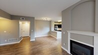 This single-floor residence is designed with an open-concept layout that connects the living, dining, and kitchen areas seamlessly. Warm wood-style flooring runs throughout the main living spaces, complemented by neutral gray walls and crisp white trim. A fireplace with a classic white mantel anchors the living area, adding a focal point to the expansive room. The kitchen is well-appointed with dark espresso cabinetry, light granite countertops, stainless steel appliances including a refrigerator and microwave, and a peninsula with a double sink that doubles as a breakfast bar. Natural light filters in through multiple windows, including a large window in the kitchen overlooking the outdoors. The bedrooms feature plush carpet flooring and ceiling fans, with the primary bedroom offering access to a walk-in closet and an adjoining bathroom. A sliding glass door leads to a private balcony with exterior views, further enhancing the sense of openness. The bathroom includes a granite-topped vanity, a tiled soaking tub with a shower combination, and wood-style flooring. Overall, the space presents a clean, modern aesthetic throughout.