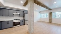 Located at 2–24 S 500 E in Salt Lake City's vibrant Capitol Hill neighborhood, this 2-bedroom, 3-bathroom unit blends modern finishes with industrial character. The open-concept living and kitchen area is anchored by a striking exposed concrete column and complementary wood beam ceiling accents, creating a loft-inspired aesthetic. The well-appointed kitchen features slate-blue cabinetry with matte black hardware, a textured tile backsplash, stainless steel appliances including a gas range, built-in microwave, refrigerator, and dishwasher, and a deep undermount sink. Light hardwood flooring flows seamlessly through the main living areas, enhancing the bright, airy atmosphere created by large windows that invite natural light throughout. The spacious primary bedroom is carpeted and features multiple windows with neighborhood views, a ceiling fan, and direct access to a dedicated bathroom with a dark vanity, ample storage, and a tub-shower combination. The second bedroom continues the light hardwood flooring and enjoys generous natural light. Three well-designed bathrooms include clean white finishes with matte black fixtures. The hallway provides efficient connectivity between rooms, completing this thoughtfully designed urban residence.