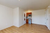 Located at 8525 163rd Ct NE in Redmond, Washington, this efficiently designed studio unit makes thoughtful use of its compact footprint. The open-plan layout combines the living, dining, and kitchen areas into a single cohesive space, finished with light-toned hardwood-style flooring that adds warmth and visual continuity throughout.

The kitchenette is tucked neatly into one corner and features warm, rich wood cabinetry, a stone-look tile backsplash, a stainless steel microwave, a compact refrigerator, and a small sink — providing essential cooking and storage functionality without overwhelming the space.

The living area is bright and open, anchored by a set of white-framed French doors that flood the room with natural light and offer views of the surrounding greenery. A built-in shelving unit integrated into the wall provides practical storage, while an overhead wall-mounted rack adds additional organizational flexibility.

The bathroom is clean and functional, featuring a tiled shower/tub surround with chrome fixtures in a crisp, all-white finish. The neutral color palette and recessed lighting throughout the unit contribute to an airy, understated aesthetic. Overall, this studio presents a well-organized and functional layout suited to efficient, comfortable living in the heart of Redmond.