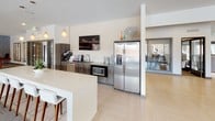 This single-floor amenity space is thoughtfully designed to accommodate a variety of social and recreational activities. The kitchenette area serves as a central hub, featuring dark wood cabinetry with dark countertops, a stainless steel side-by-side refrigerator with water dispenser, a built-in microwave, and a wall-mounted television. A white counter with bar seating and pendant lighting completes the space, while light herringbone-patterned flooring extends throughout, creating a clean, contemporary aesthetic.

Adjacent to the kitchenette, an open dining and lounge area offers flexible seating with high-top tables and chairs arranged near large windows that frame outdoor views and fill the space with natural light. A bold magenta accent wall with built-in shelving adds a vibrant design element to this zone.

A dedicated lounge area features plush sofas arranged around a coffee table, anchored by a richly colored area rug. Textured blue-gray wallcovering, a deep burgundy accent wall, and a wall-mounted TV create an inviting, intimate atmosphere enhanced by a statement pendant light fixture.

The game room rounds out the space with a full-length shuffleboard table as its centerpiece, complemented by matching textured wallcovering, bold artwork, and additional casual seating, making it an ideal setting for entertainment and recreation.