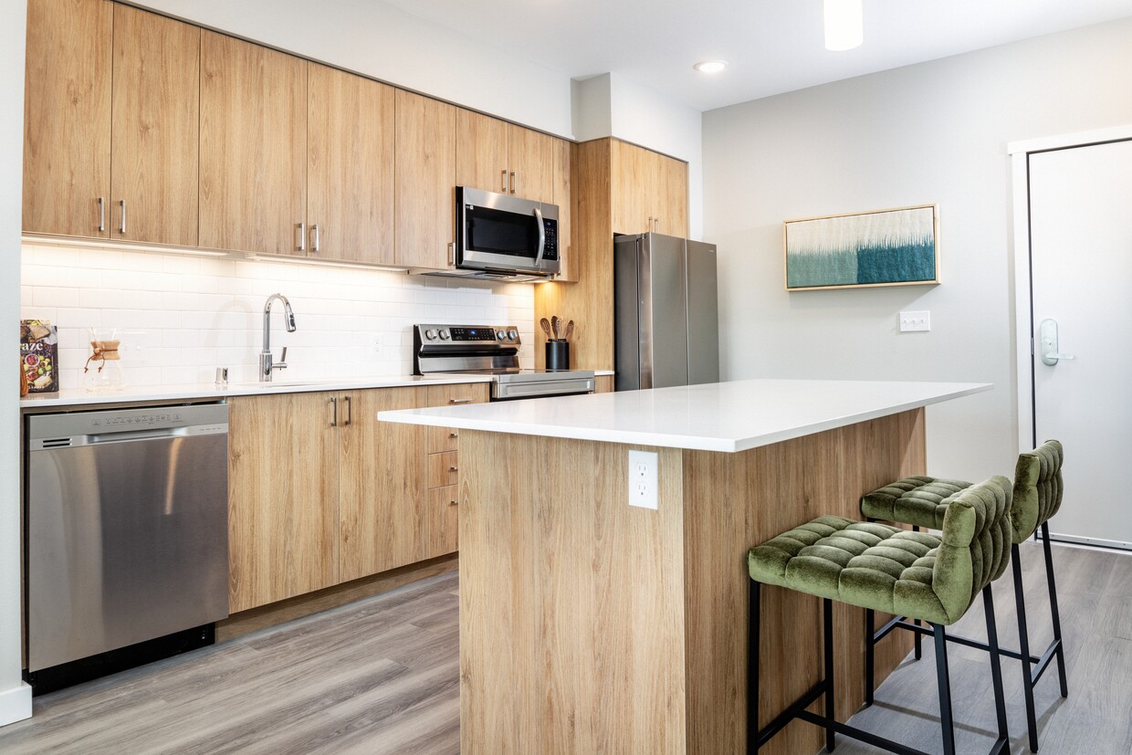 Cocina con gabinetes de roble, encimeras de granito blanco, protector contra salpicaduras de azulejos blancos y electrodomésticos de acero inoxidable - Avalon Redmond Campus