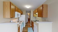 This single-floor residence at Cooper Creek offers a practical and well-organized layout with a consistent design aesthetic throughout. The galley-style kitchen is efficiently arranged, featuring warm oak cabinetry on both upper and lower sections, white appliances including a refrigerator, electric range, built-in microwave, and dishwasher, along with light countertops and a single-basin sink. Wood-look plank flooring runs through the kitchen, adding durability and visual continuity.

The living areas are finished with the same wood-look flooring, neutral beige-toned walls, and clean white baseboards, creating a bright and cohesive atmosphere. Natural light enters through windows fitted with horizontal blinds, offering views of surrounding greenery. The open layout of the living spaces allows for flexible furniture arrangements, and multiple doorways connect the rooms in a functional flow.

Bedrooms provide a softer feel with plush carpeting underfoot and multiple windows that bring in ample natural light. The neutral color palette throughout the home maintains a calm, move-in-ready environment. Overall, the space combines practical functionality with a clean, understated design suitable for everyday living.