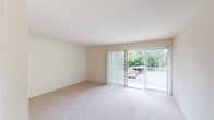 This single-floor residence offers a well-organized layout with a neutral, light-filled aesthetic throughout. The living area is generously proportioned, featuring soft wall-to-wall carpeting and large sliding glass doors fitted with vertical blinds that open directly onto a balcony overlooking mature trees and outdoor surroundings, bringing in abundant natural light and pleasant views.

Adjacent to the living space, a dedicated dining area features a pendant light fixture and continues the carpeted flooring, connecting seamlessly to the rest of the unit. The galley-style kitchen is efficiently designed with light wood cabinetry lining both sides, white appliances including a refrigerator, electric range, and over-the-range microwave, complemented by a stainless steel sink and white countertops. A separate pantry or storage closet is accessible directly from the kitchen, providing additional organizational space. The kitchen flooring consists of light-toned vinyl tile.

The bedrooms are well-sized, each finished with soft carpeting and windows that allow natural light to filter in. The bathroom features a wide vanity with a large mirror, under-sink cabinetry, and clean white finishes throughout, creating a bright and functional space.