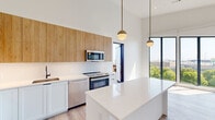 Unit 535 at 282 Bremen Street in Boston's East Boston neighborhood is a thoughtfully designed one-bedroom, one-bathroom residence that balances modern aesthetics with functional living. The open-concept layout is anchored by soaring ceilings that amplify the sense of space, while light wood-tone flooring runs throughout, providing warmth and continuity.

The kitchen is a standout feature, showcasing a clean two-tone design with white lower cabinetry and natural wood upper cabinets extending nearly to the ceiling for ample storage. A white quartz waterfall island serves as both a prep surface and casual dining area. Stainless steel appliances — including a refrigerator, range, microwave, and dishwasher — complete the suite. Pendant globe lights with brass accents add a contemporary touch, and a large floor-to-ceiling window floods the space with natural light and city views. A private deck is accessible directly from the main living area.

The bedroom is a serene, well-proportioned retreat with high ceilings, crisp white walls, and the same wood-tone flooring. A dedicated closet provides practical storage.

The bathroom features a clean, modern design with white subway wall tiles, a combined tub and shower with matte black fixtures, and distinctive blue hexagonal floor tiles that add a subtle design accent.