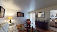 This single-floor residence offers a thoughtfully organized layout that connects living, dining, kitchen, and sleeping areas in a cohesive flow. The living room serves as the heart of the home, featuring warm hardwood-style flooring, a textured ceiling, and a sliding glass door dressed with vertical blinds that allows natural light to fill the space. A dark wood credenza, circular glass coffee table, and a multicolored area rug contribute to the room's balanced, casual aesthetic. Framed wall art adds visual interest throughout.

A partial dividing wall separates the living area from the kitchen, which is fitted with warm wood cabinetry, laminate countertops, and white appliances including a refrigerator, dishwasher, and electric range. Light flooring ties the kitchen visually to the rest of the home.

The bedroom offers a quieter retreat, finished with plush carpeting and neutral walls. A dark-framed bed and nightstand provide a grounded, restful atmosphere, complemented by a trio of framed prints above the headboard.

The bathroom includes a vanity with wood cabinetry and granite-style countertop, a large mirror, and a tub-shower combination with a curtain enclosure, finished with hardwood-style flooring.