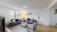 This thoughtfully designed single-floor residence offers a cohesive blend of modern style and everyday functionality. Light wood-tone flooring flows throughout, tying each room together with a warm, contemporary feel.

The living room serves as the heart of the home, featuring large windows that invite abundant natural light and offer views of the surrounding greenery. The space comfortably accommodates dual sofas and a modern accent chair arranged around a sleek coffee table, creating an inviting area for relaxing or entertaining. A textured ceiling adds subtle character throughout the home.

Adjacent to the living area, the dining space is bright and welcoming, with wall-mounted shelving for decorative accents and a round mirror that enhances the sense of openness.

The kitchen is outfitted with white cabinetry, white quartz countertops, and a full suite of stainless steel appliances, including a refrigerator, range, and over-the-range microwave. A dedicated in-unit laundry closet with a full-size washer and dryer adds everyday convenience.

Both bedrooms are comfortably sized, filled with natural light through wide windows, and offer room for a bed, storage, and a workspace. The full bathroom features clean white finishes, a combined tub and shower, and matte black fixtures for a modern touch.