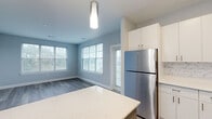 This single-floor, two-bedroom, two-bathroom residence in East Providence, Rhode Island offers a well-designed layout with modern finishes throughout. The open-concept kitchen serves as a central hub, featuring white cabinetry, a marble-style tile backsplash, quartz countertops, a large island with a contrasting blue base, stainless steel appliances, and pendant lighting. Wood-look flooring flows through the kitchen and living areas, while large windows and a glass-paneled exterior door flood the living space with natural light and offer views of the surrounding neighborhood.

Both bedrooms are carpeted and generously sized, with neutral gray walls creating a calm, versatile backdrop. One bedroom includes a walk-in closet fitted with wire shelving and hanging systems, providing practical storage. The two bathrooms mirror each other in style, each featuring wood-look tile flooring, light wood-toned vanities with white quartz countertops, and tub-shower combinations. Clean white panel doors and crisp white trim are consistent throughout, reinforcing the home's cohesive, contemporary aesthetic.