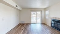 Located at 537 Pepper Dr in Hanford, CA, this single-story, one-bedroom, two-bathroom residence offers a well-designed layout that maximizes its compact footprint. The open-concept living and kitchen area forms the heart of the home, where warm wood-look plank flooring flows throughout. The kitchen stands out with rich medium-toned wood cabinetry, granite countertops, a double stainless steel sink set into a peninsula, recessed lighting, and black appliances including a refrigerator and range. A ceiling fan with light fixture adds comfort to the adjacent living area, which features a tile-surround fireplace as a focal point and a sliding glass door opening to a private balcony, allowing abundant natural light to fill the space. The bedroom offers plush carpeting, a bright window with outdoor views, and a closet. Both bathrooms echo the kitchen's design with granite vanity countertops and warm wood cabinetry. One bathroom includes a shower/tub combination. Additional features include central HVAC with vents throughout and a textured ceiling. The overall aesthetic is clean, neutral, and move-in ready, providing a comfortable and functional living environment.
